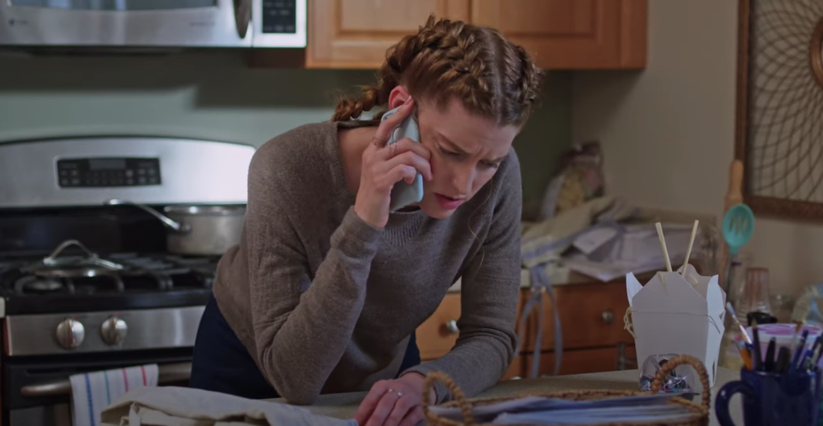 Felicity looks distressed as she stands hunched over a slightly unkempt kitchen countertop on the phone.